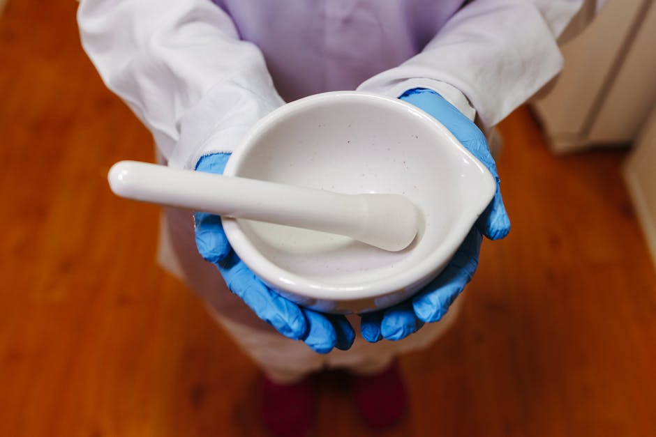 Pharmacist holding a white mortar and pestle, wearing blue gloves and lab coat indoors.