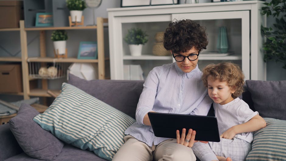 A woman and her son sitting on a couch, using a tablet together at home.