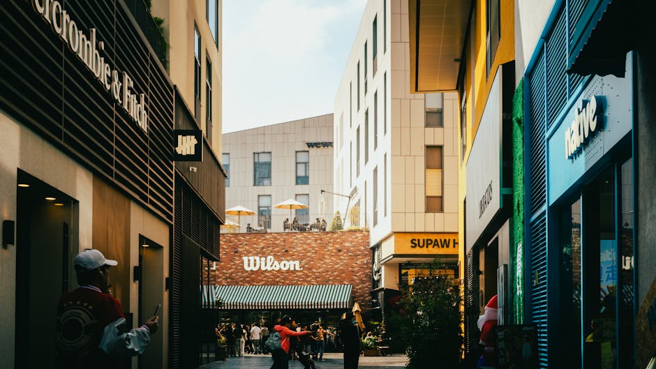 Urban alley lined with modern shops and signs, showing busy city life with people and vibrant storefronts.