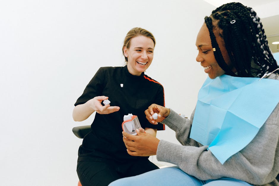 Smiling dental doctor in black uniform talking with ethnic female patient sitting in dental chair and showing model of teeth in modern clinic