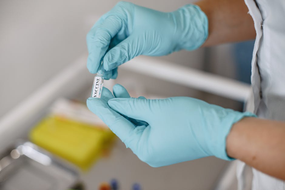 Close-up of hands in gloves holding a vaccine vial in a clinical setting.