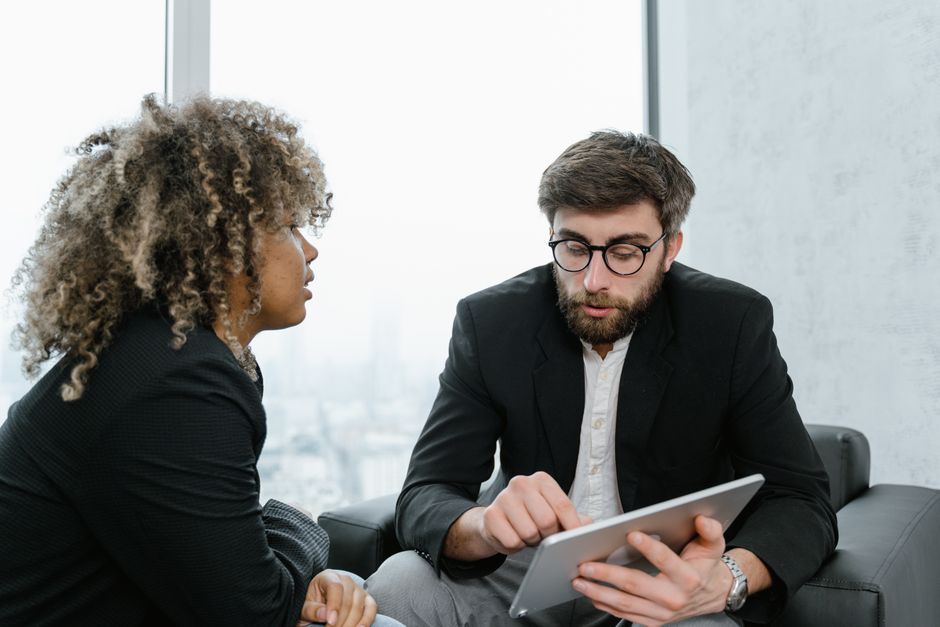 A focused business meeting between two professionals discussing data on a tablet indoors.
