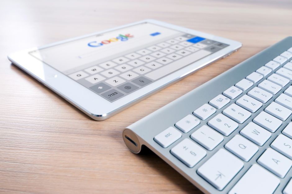 A modern tablet displaying a search engine logo next to a wireless keyboard on a wooden desk.