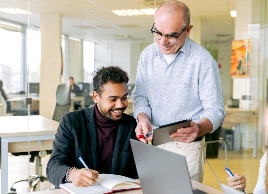 Two colleagues engaged in a discussion at a modern workspace, using digital devices and notes.