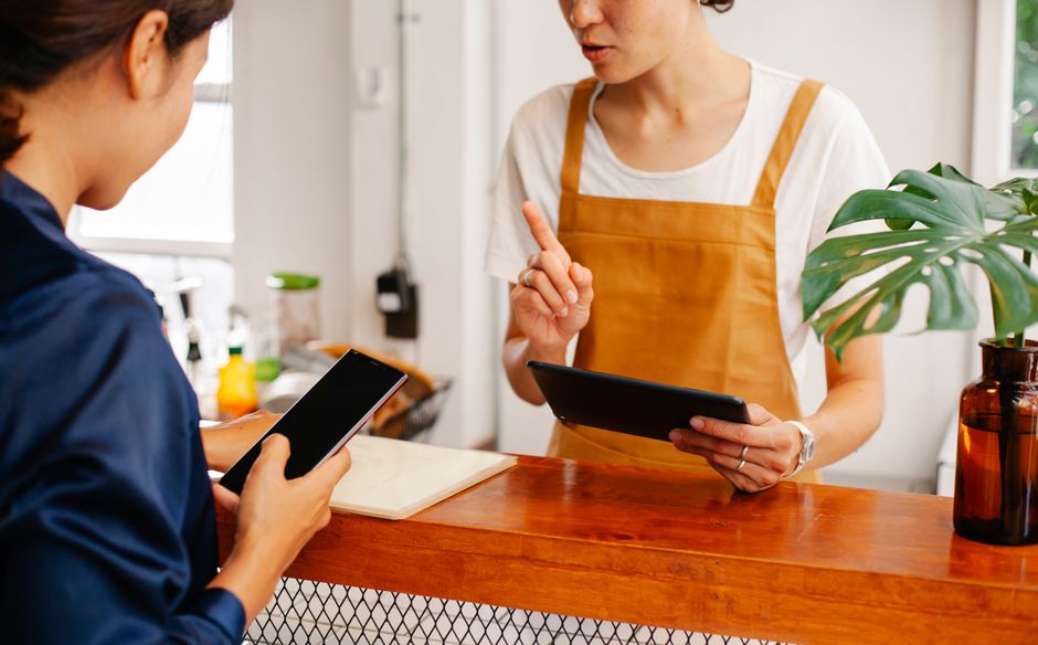 Crop anonymous female employee with finger up speaking with partner touching black screen on cellphone in cafe